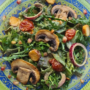 Colorful green salad with pine nuts, mushrooms, sun-dried tomatoes, and tahini sauce